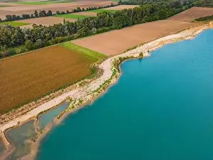 Water Body Prints: Fields and a forest next to the shore of an artificial lake with turquoise water in fall seen from above by a drone