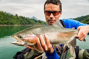 Trout Prints: Fisherman with orange sunglasses holding the catch of Rainbow trout (Oncorhynchus mykiss) sitting on bellyboat