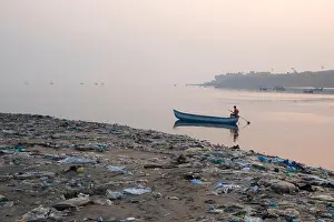 Problems Prints: Fisherman paddles his boat past piles of plastic garbage and other rubbish on Versova Beach