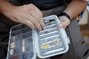 Bait Prints: Fisherman selecting a hand tied small feather fly from a handheld white plastic folding tackle box in a close up view