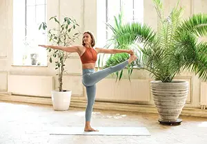 Barefoot Prints: Fit adult woman on mat in pose and looking away while practicing yoga in spacious room at home