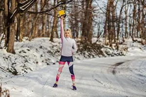 Practicing Prints: Fit sportswoman lifting kettlebell while standing on snowy path in nature at winter