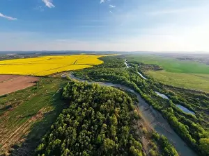 Flight through majestic river, lush green forest and blooming yellow rapeseed fields at sunset time. Landscape photography