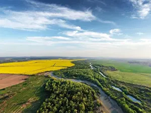 Flight through majestic river, lush green forest and blooming yellow rapeseed fields at sunset time. Landscape photography