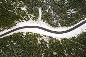 Flight over the winter mountains with road serpentine and snowy forest. Top down view. Landscape photography