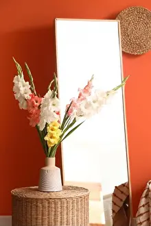 Holiday Home Prints: Floor mirror, wicker table and vase with gladiolus flowers in interior of living room
