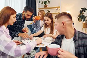 Sincere Prints: Focused at puzzle game. Group of friends have party indoors together