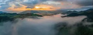 Fog envelops the mountain forest. The rays of the rising sun break through the fog. Aerial drone view