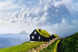Foggy morning view of a house with typical turf-top grass roof and blue cloudy sky in the Velbastadur village on Streymoy island, Faroe islands