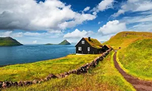 Foggy morning view of a house with typical turf-top grass roof and blue cloudy sky in the Velbastadur village on Streymoy island, Faroe islands, Denma