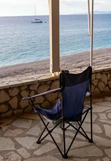 Sky Clouds Prints: A folding chair on the covered patio of a seaside building with a great view of the sea and sunset sky clouds