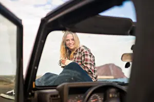 Soul Prints: freedom and vacation concept for beautiful blonde caucasian young woman sitting down on the nose of a off road black