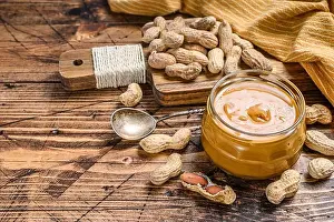 Creamy Prints: Fresh made creamy Peanut Butter in a glass jar. Wooden background. Top view. Copy space