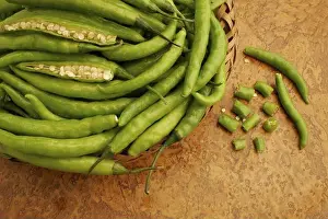 Lies Prints: Fresh green chillies or pepper vegetable kept in cane bowl with two opened pieces showing white seeds