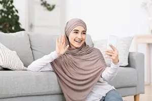 Free Space Prints: Friendly Arabic Girl In Headscarf Making Video Call Via Smartphone At Home