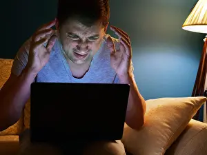 Exhausted Prints: Frightened or angry man with laptop on a sofa. Evening time