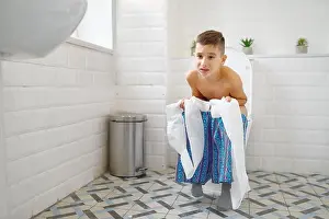 Frowning Prints: Frowning little boy holding paper sitting on toilet and trying to poop