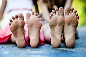 Sisters Prints: Funny feet of two girls sitting on a pavement in green park