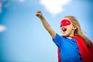 Superhero Prints: Funny little girl playing power super hero over blue sky background. Superhero concept