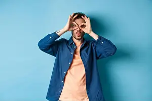 Unshaved Prints: Funny young man looking through hand binoculars and say wow
