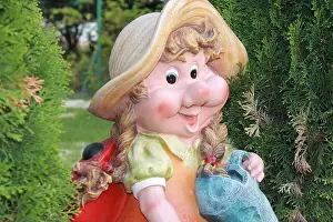 Kitsch Prints: Garden figure is dwarf woman close-up between green trees, the gnome has big smile