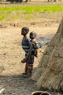 Nigeria Prints: GHANI, GHANA - JAN 14, 2017: Unidentified Ghanaian little girl carries a baby on her back in the Ghani village