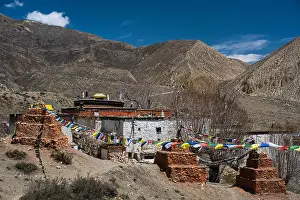 Tibetan Prints: Ghar Gompa of Lo Gekar with prayer flags in front of mountain landscape