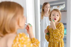 Siblings Prints: Girl applying lipstick looking in mirror at home