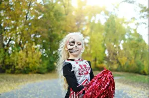 Frightening Prints: A girl in a cheerleader costume and half-face makeup in the form of a skeleton celebrates Halloween