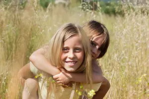 Sister Prints: Girl giving friend piggy back in field