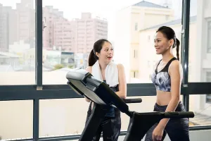 Reduce Prints: girl meet and talking to her friend who walking on treadmill machine and enjoys the workout together in the gym