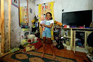 Lengths Prints: Girl, smiling, holding a doll in an apartment in a slum or favela