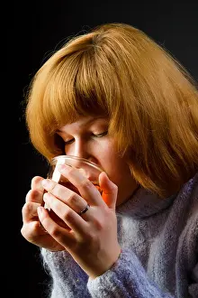 Black Cap Prints: girl in a sweater on a black background drinking tea from a transparent cup. portrait