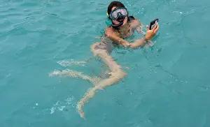 Tropical Waters Prints: Girl uses her phone to take pictures of turtles, Curaçao