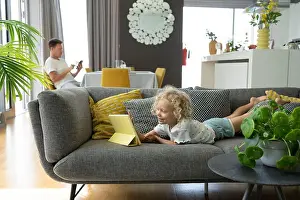 Curly Hair Prints: Girl using tablet PC lying on sofa with father in living room at home