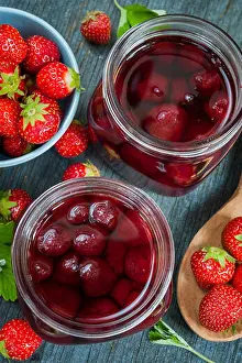 Strawberries Prints: Glass jars with homemade strawberry preserve and fresh strawberries in bowl from above on blue rustic wood background