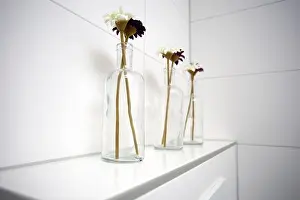 Gerbera Prints: Three glass vases with daisies near white tiled wall in the bathroom