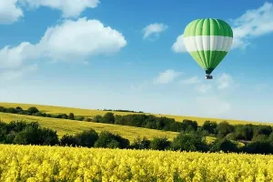 Airship Prints: Green balloon under yellow rape field on blue sky background. Landscape photography