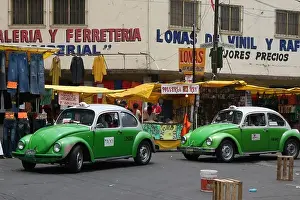 Two green and white beetle taxis driving through a market in Mexico City, Mexico, South America