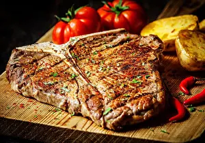 Lean Prints: Grilled T-bone steak seasoned with spices and fresh herbs served on a wooden board with fresh tomato