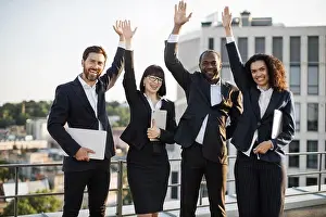 Multicultural Prints: Group of diverse colleagues celebrating shared corporate success and raising hands in air outdoors