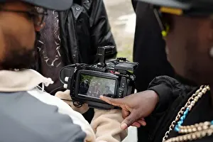 Sleeve Prints: Group of individuals gathered around camera while reviewing shot taken during outdoor location shoot