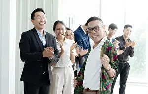 A group of people are smiling and clapping, with one man in a floral shirt standing out. Scene is happy and celebratory