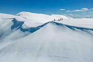 A group of people stand on a snowy mountain top with a blue sky and clouds in the background. Carpathian mountain range