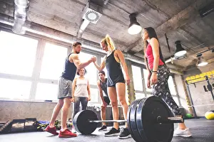 Barbell Prints: Group of young fit people motivating woman weightlifting in gym
