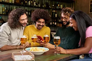 Group of young people watching at mobile in a bar. This four multi-ethnic friends are smiling