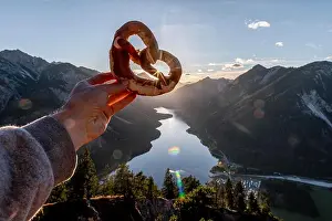 Mountain Lake Prints: Hand holding Bavarian pretzel in front of Alpine panorama