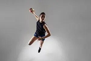 Throwing Prints: Handball player posing on light gray background. Girl jumping with ball