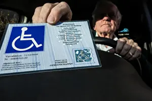 Authorized Prints: Handicapped elderly man placing EU parking card for people with disabilities – Blue Badge - behind windscreen of car