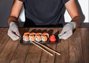 Chopstick Prints: Hands in rubber gloves serve sushi on a wooden table. Sushi menu